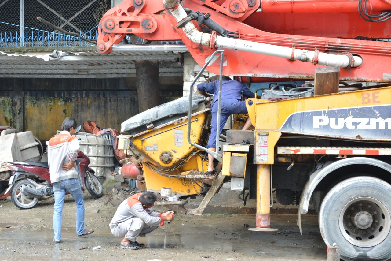 Construction workers fixing a cement mixer truck outdoors, showcasing teamwork and machinery maintenance.