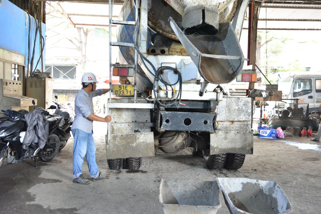 A worker in a hard hat inspects a cement mixer truck inside a garage, highlighting industry and maintenance.